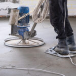Ramming and grinding of semi-dry floor screed by a machine with a rotating disk for leveling. Construction of a concrete floor in the house, a master with special equipment.